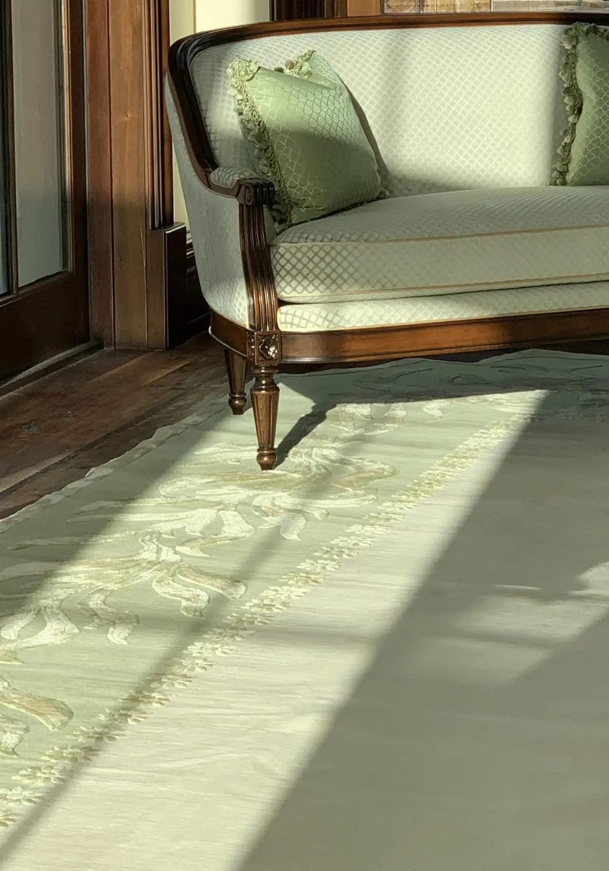 Elegant settee and light green pillows on a floral mint green rug in bright sunlight.